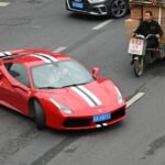 Red ferrari driving on a street with other vehicles.