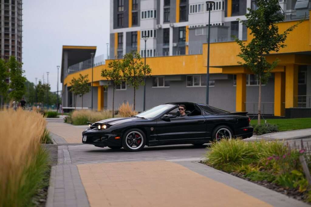 A black car driving down a street next to tall buildings