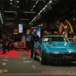A teal classic car drives across an auction stage.