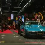 A teal classic car drives across an auction stage.