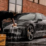 man in black t-shirt and black pants doing water splash on black coupe during daytime