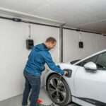 Man charging white electric car in garage.