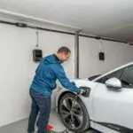 Man charging white electric car in garage.