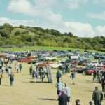 Crowd gathered at a car show with many vehicles.