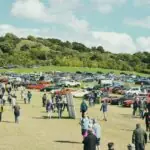 The Real Story of Car Week 2026 Isn't a Car. It's a Fence. Crowd gathered at a car show with many vehicles.
