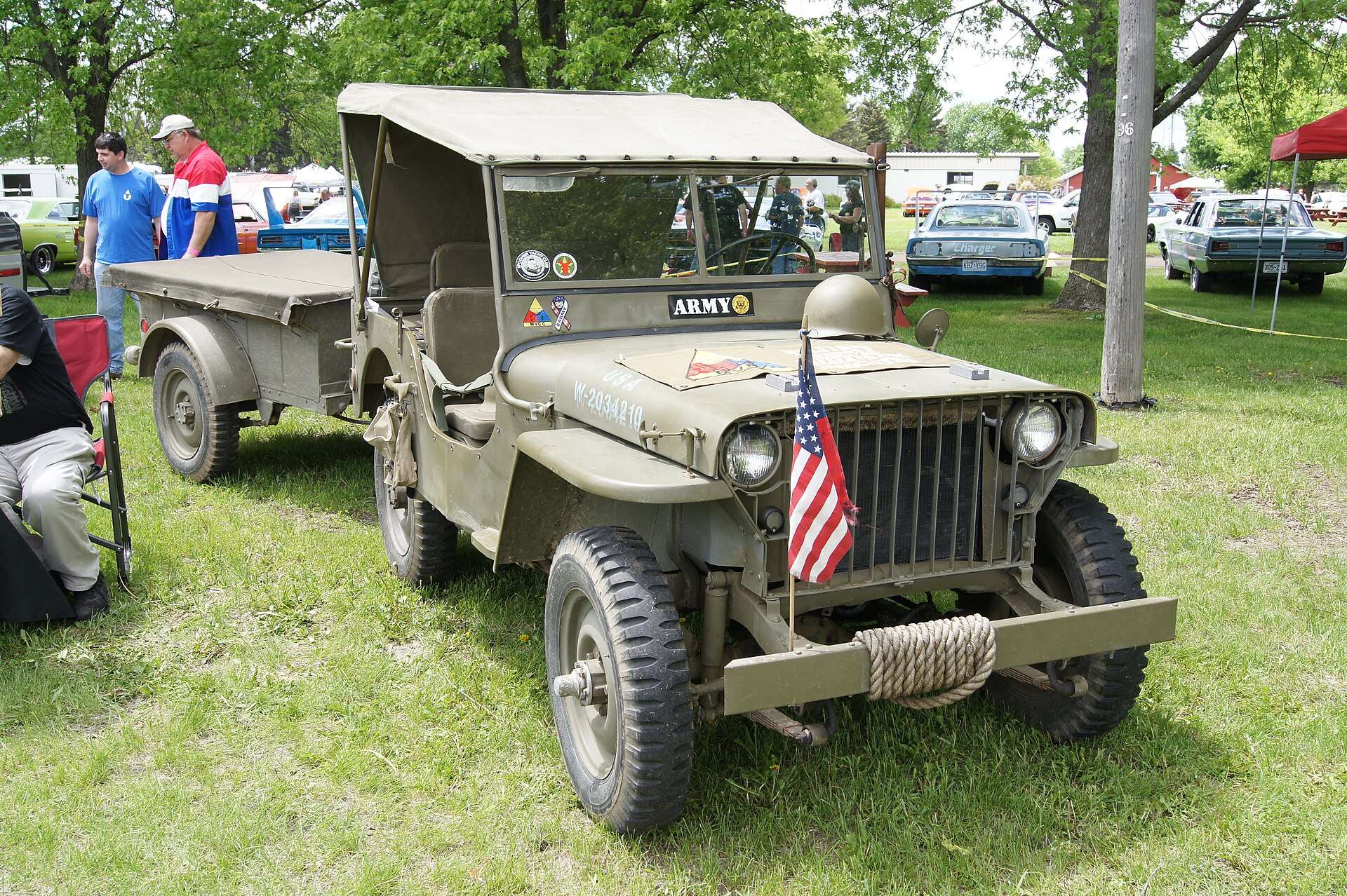 Early Willys MB jeep with welded slat grille and trailer at a car show