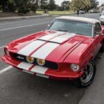 Red 1967 Shelby GT500 fastback with white racing stripes, front three-quarter view
