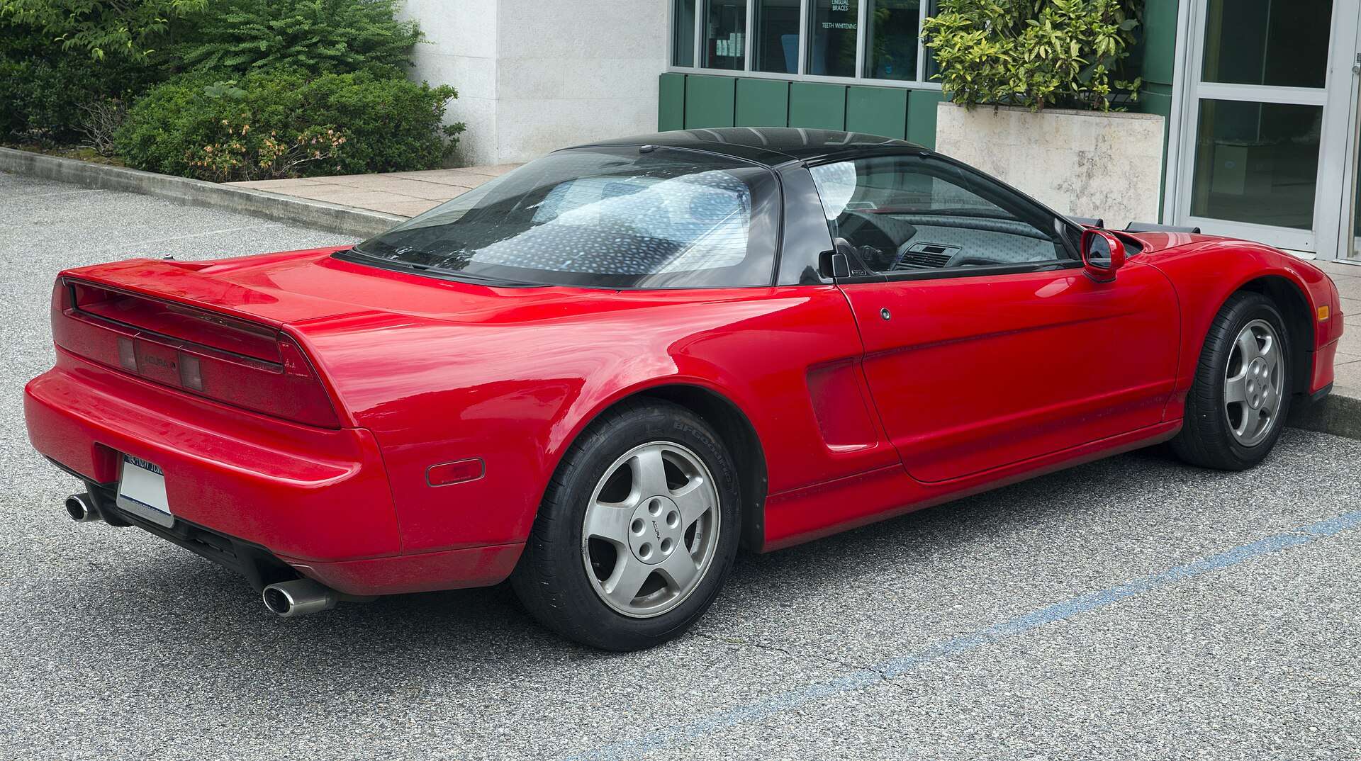 Rear three-quarter view of a red 1991 Acura NSX showing the full-width taillight bar, rear spoiler and black roof