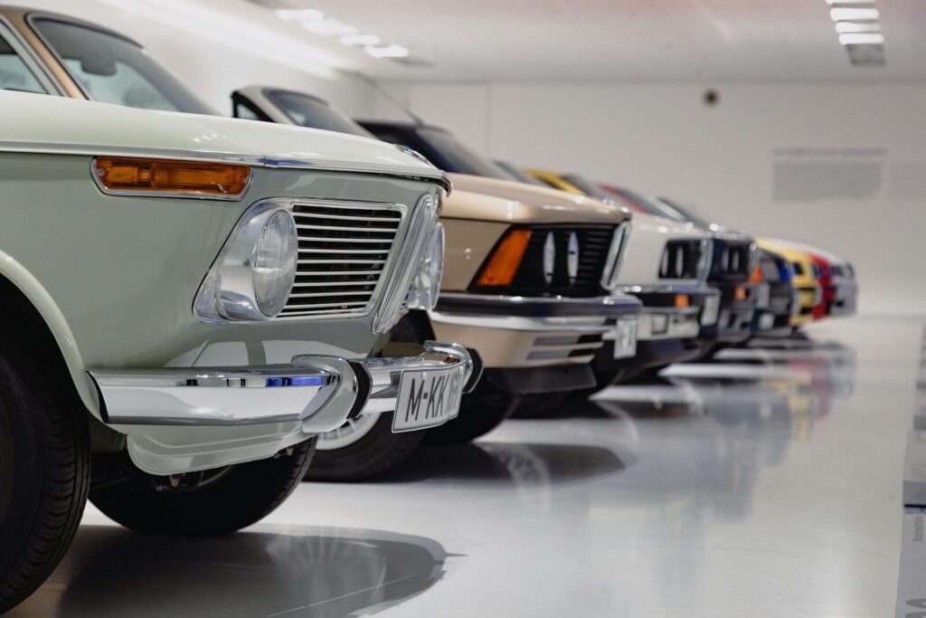 A row of classic collector cars displayed nose-to-tail in a private showroom setting