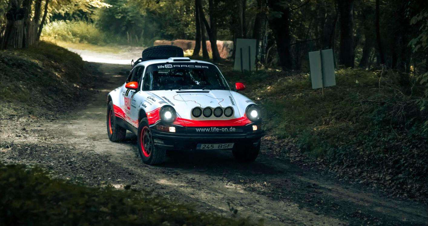 Air-cooled Porsche 911 built as a safari rally car driving on a forest gravel road