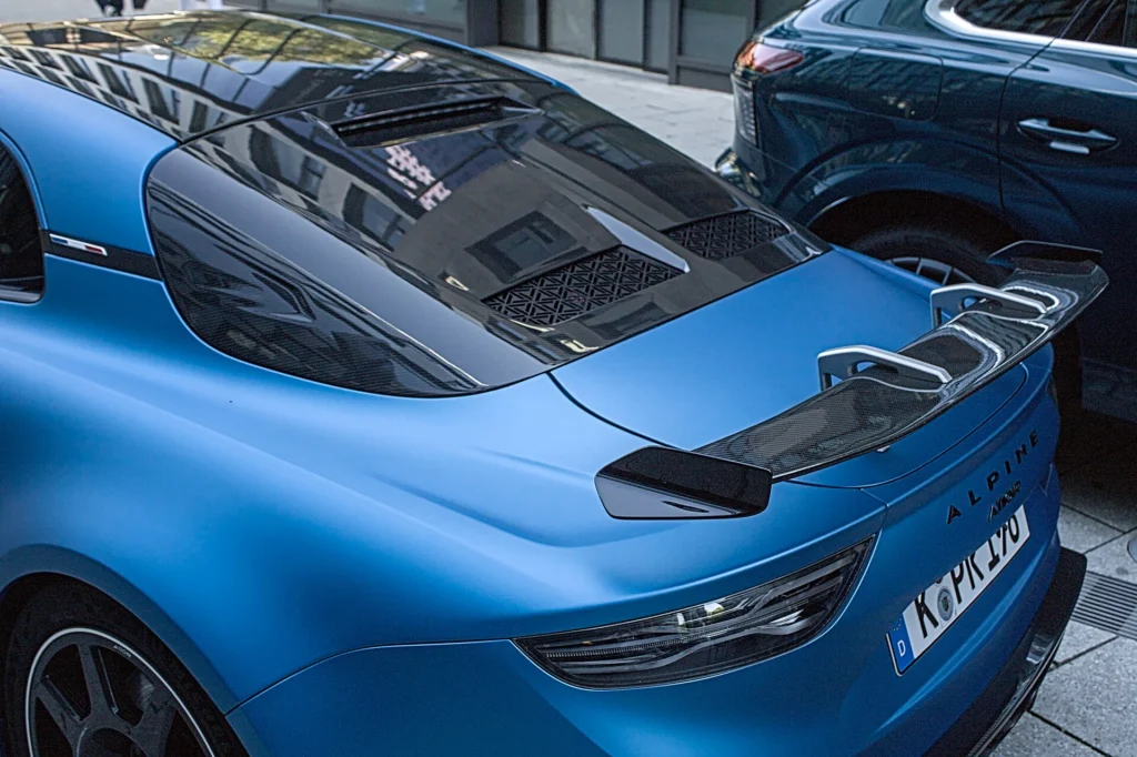 Rear three-quarter view of a matte blue Alpine A110 R showing its swan-neck rear wing