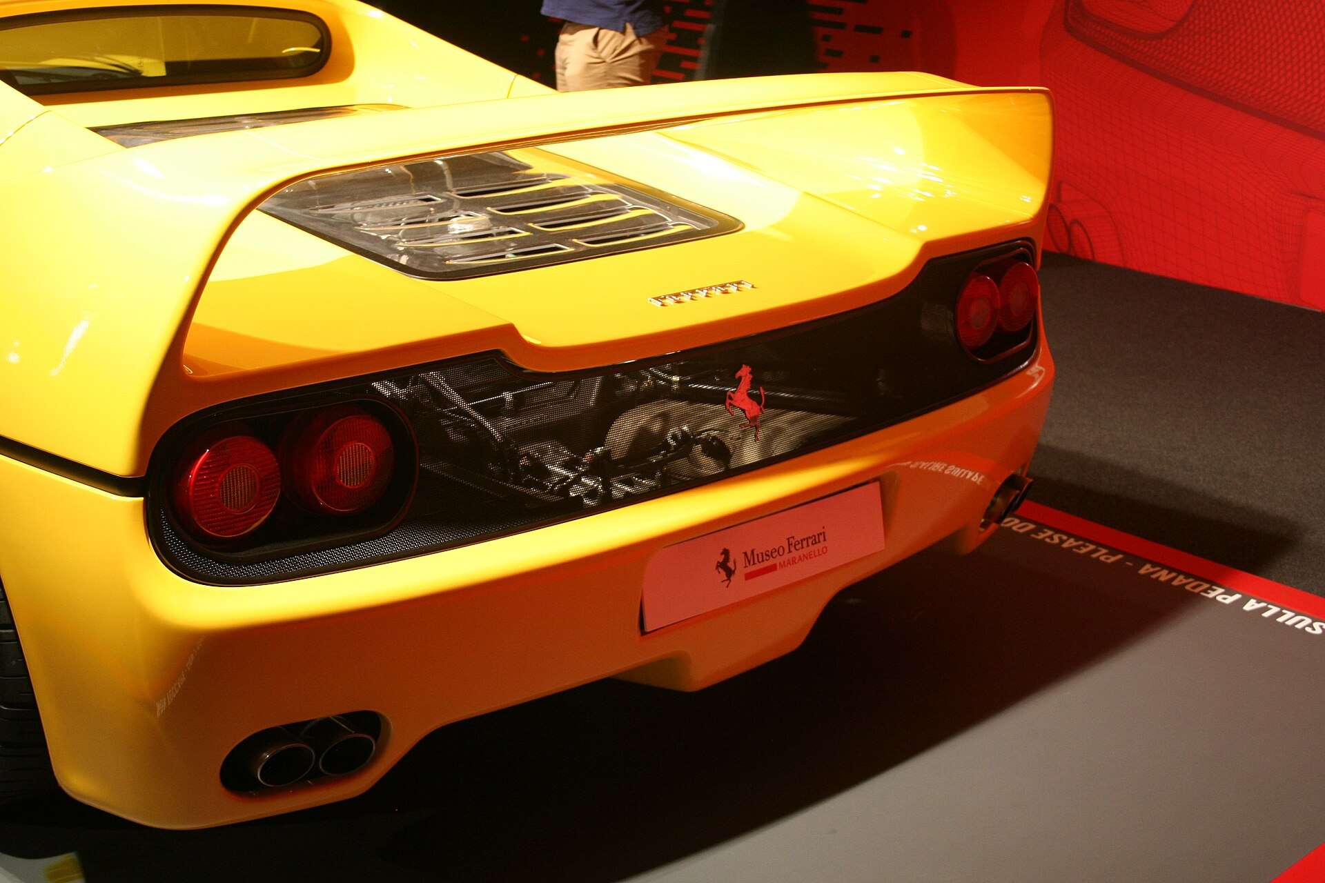Rear view of a yellow Ferrari F50 showing the exposed V12 engine bay and quad taillights