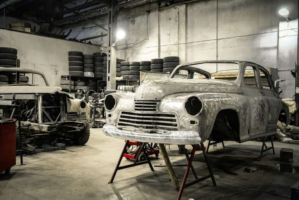 A vintage sports car body stripped to bare metal on a stand during a period-correct restoration