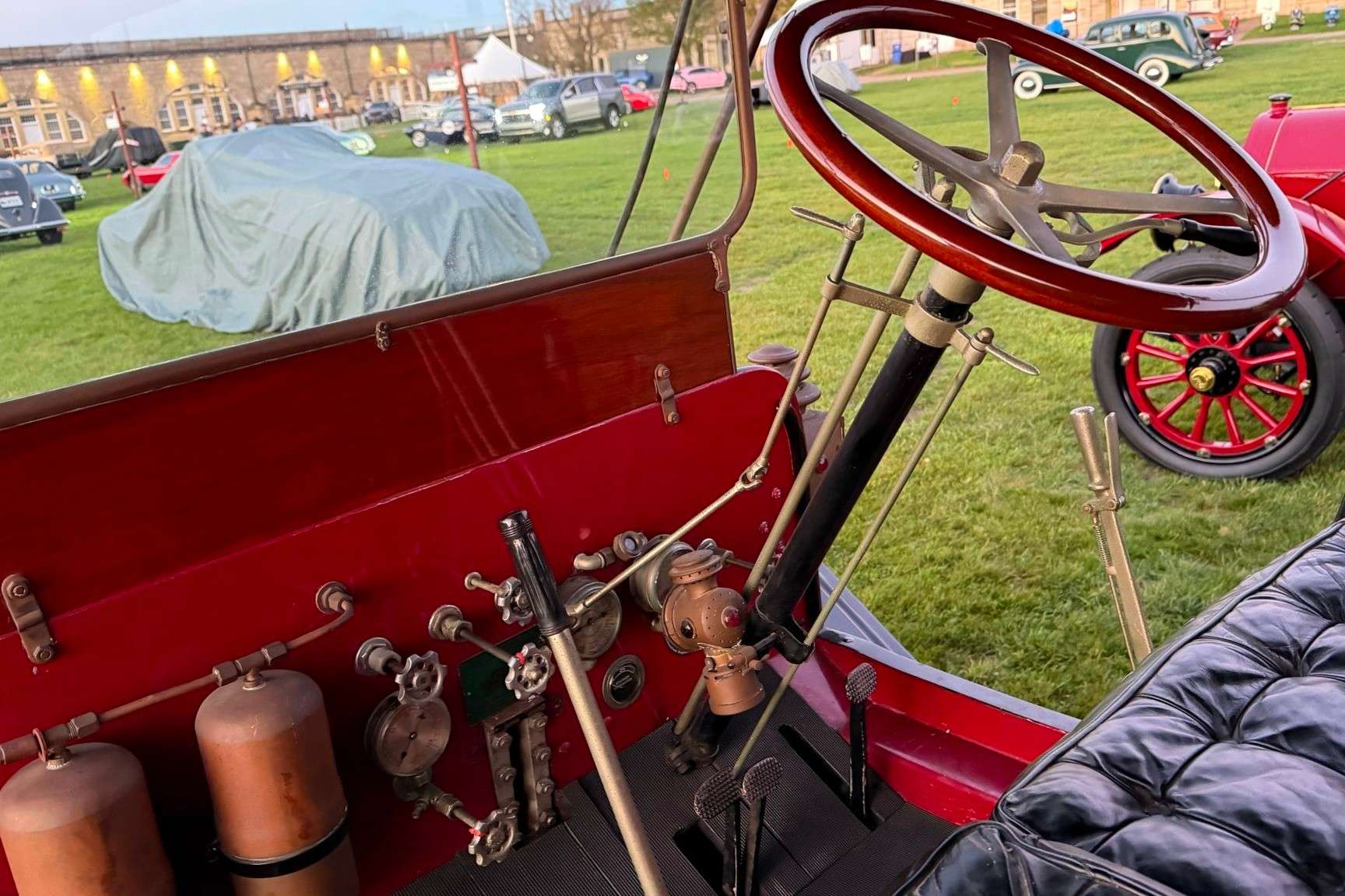 Driver’s controls of the 1913 Stanley Mountain Wagon with a wood-rimmed steering wheel, valves and pressure gauges on a red dashboard panel