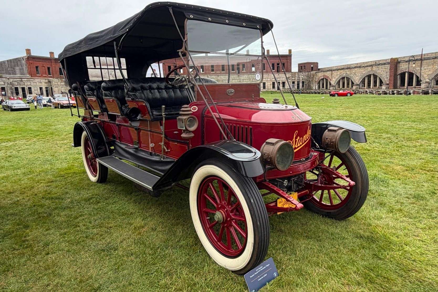 Front three-quarter view of the red 1913 Stanley Mountain Wagon on grass at Audrain Motor Week with its black soft top raised