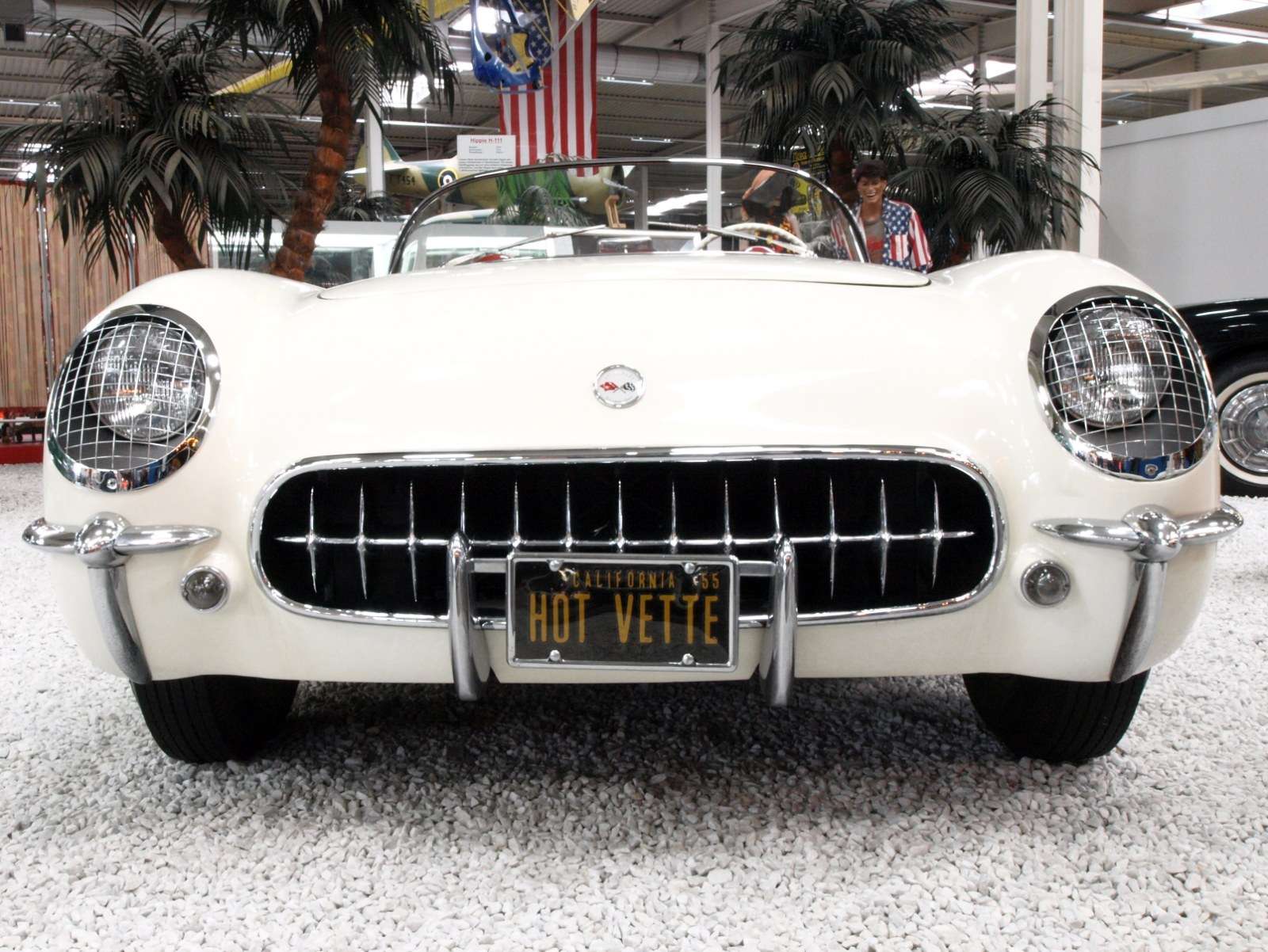 White 1955 Chevrolet Corvette roadster with a mesh grille, the Thunderbird’s main rival, on display indoors