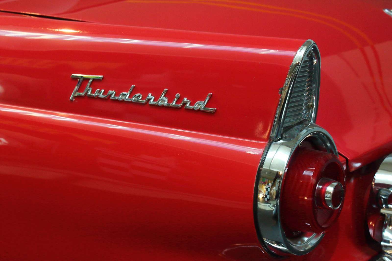 Close-up of the Thunderbird script and chrome taillight surround on the rear fender of a red 1955 Ford Thunderbird