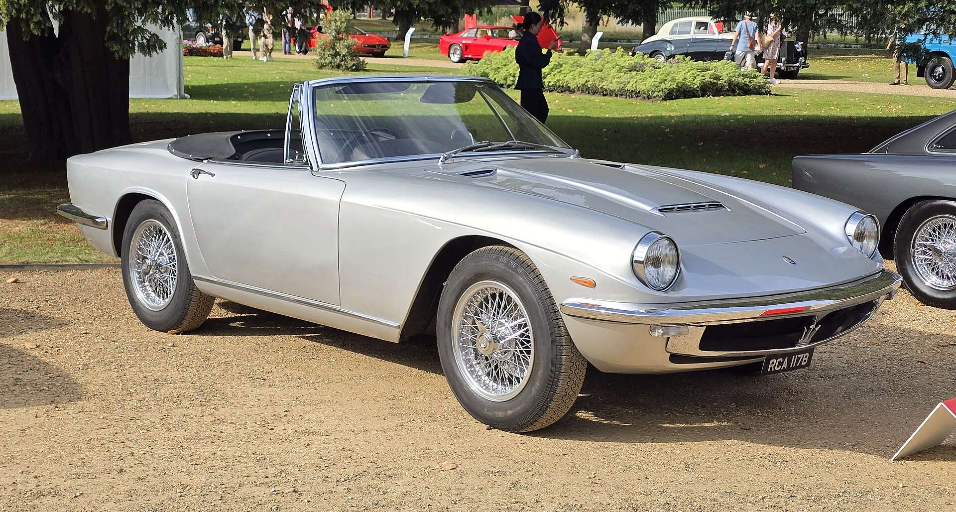Silver 1964 Maserati Mistral Spyder with wire wheels and the top down on gravel at a concours lawn