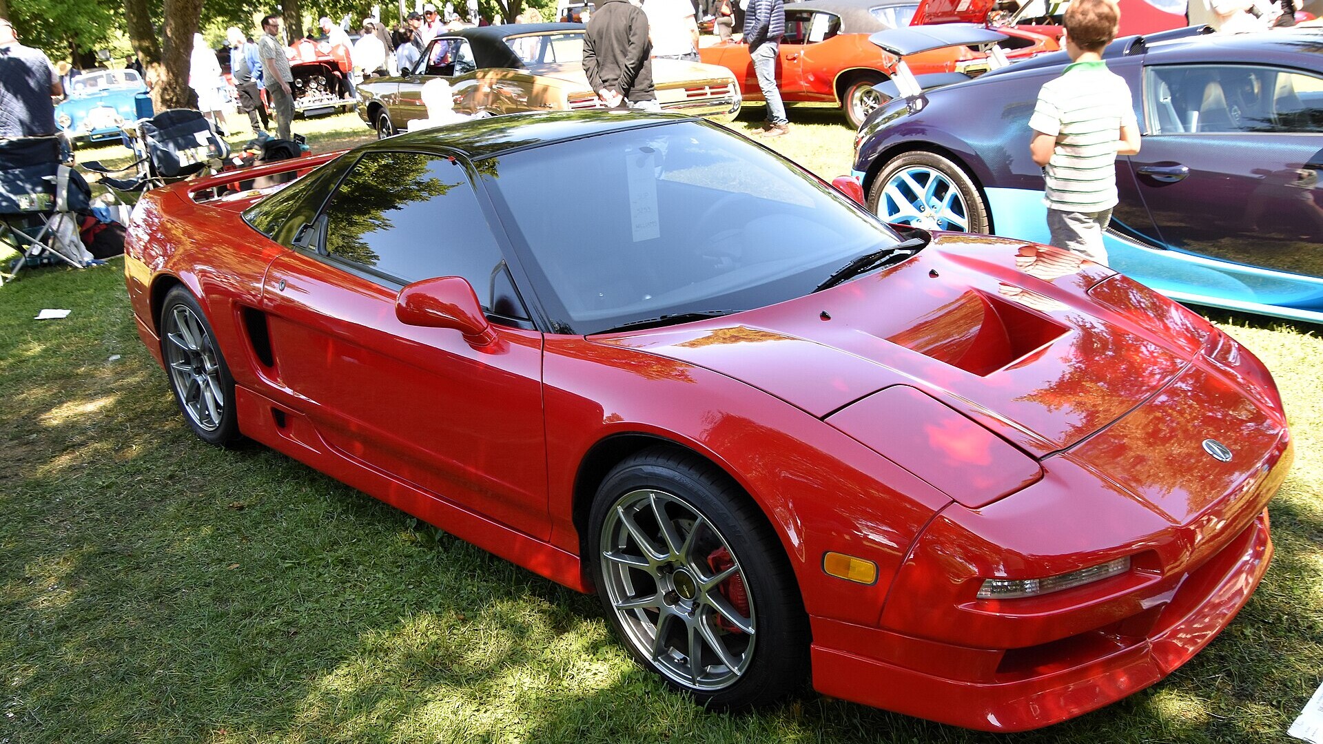 Red first-generation Acura NSX with aftermarket wheels parked on grass at an outdoor car show