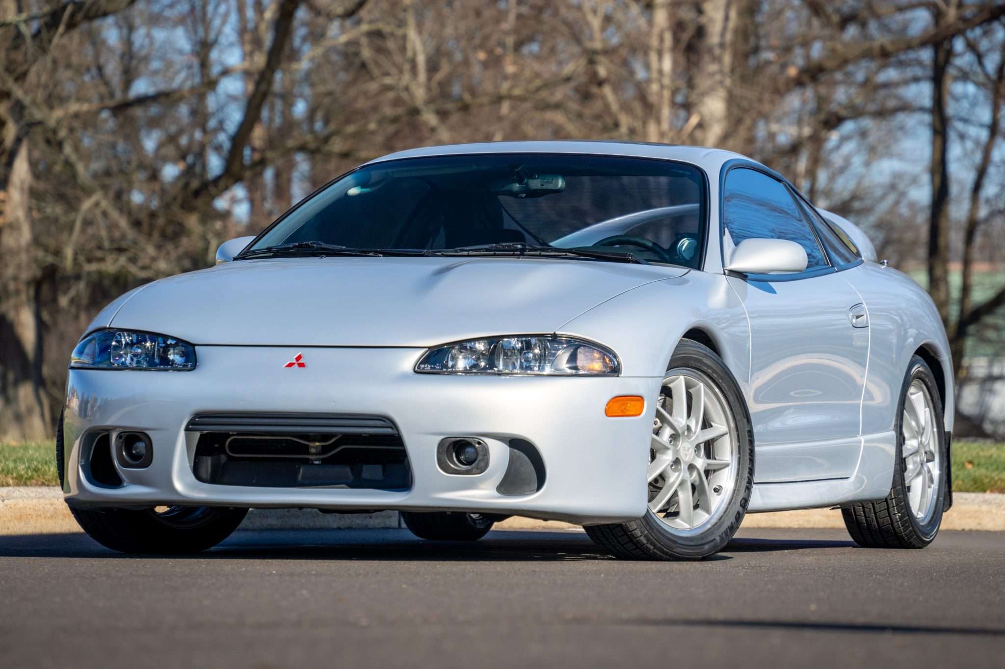 Silver 1999 Mitsubishi Eclipse GSX coupe photographed from the front three-quarter angle against bare trees