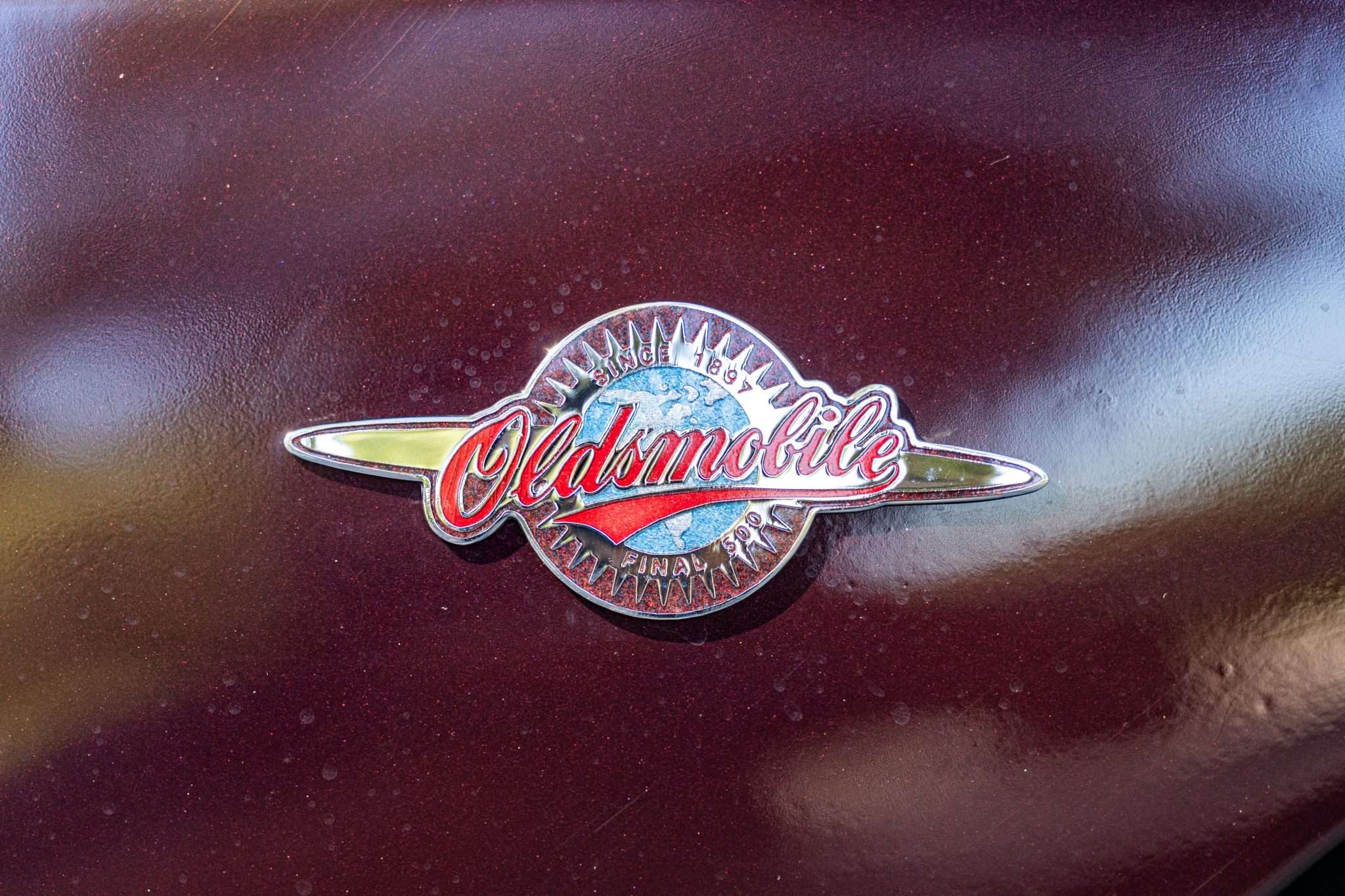 Round red, chrome and blue Oldsmobile Aurora Final 500 badge reading Since 1897 on the fender of a 2003 Aurora