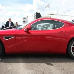 Side profile of a red Alfa Romeo 8C Competizione coupe parked outdoors on grass