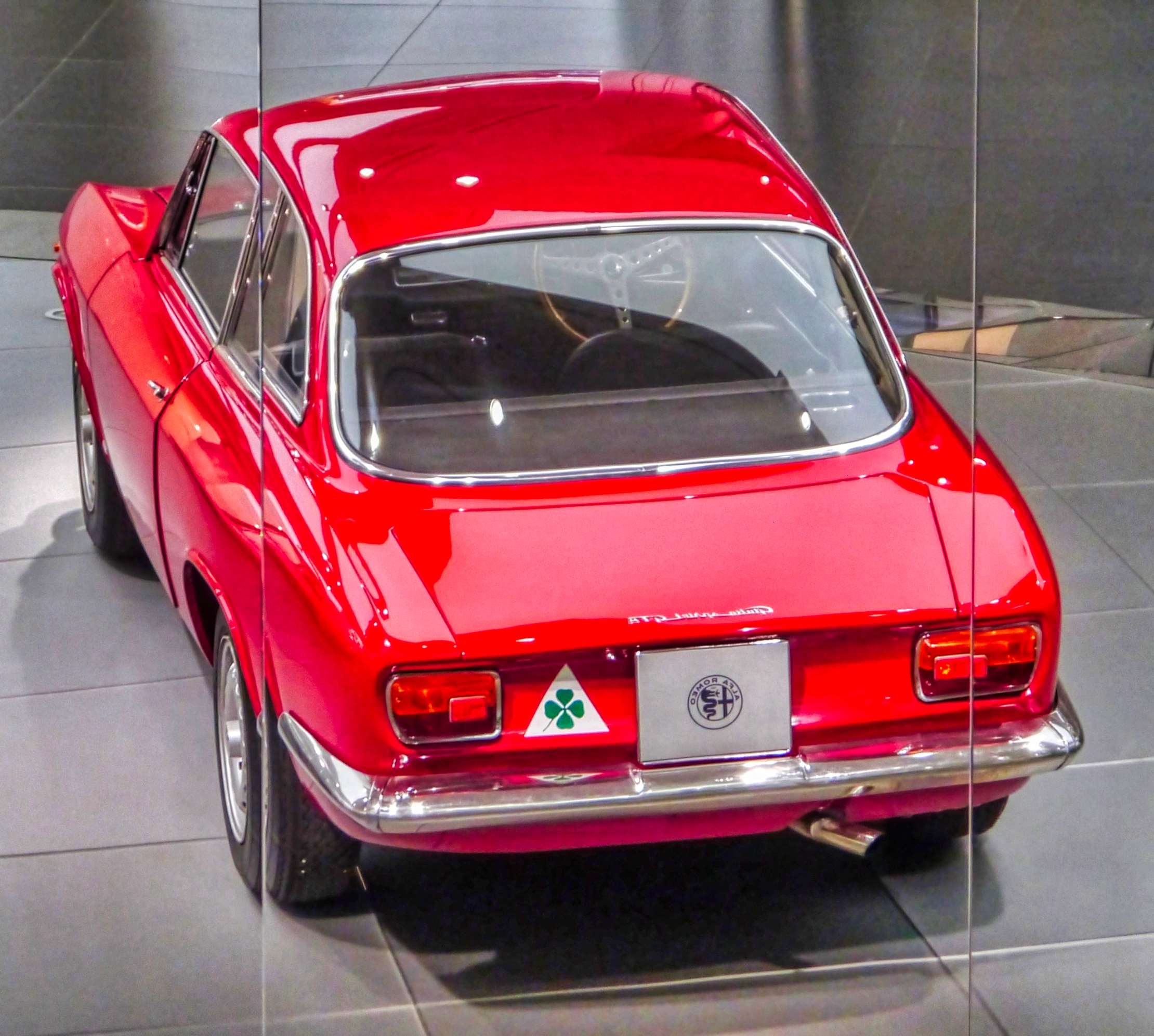 Rear view of a red 1965 Alfa Romeo Giulia Sprint GTA with Quadrifoglio badge and chrome bumper in a museum