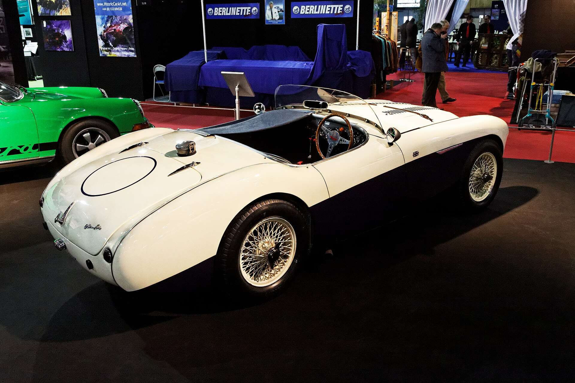 Rear three-quarter view of a white and dark blue 1955 Austin-Healey 100S on display with wire wheels and no bumpers