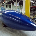 Blue Flame rocket car, a long steel-blue streamliner, seen from the front three-quarter angle on display at the Auto & Technik Museum Sinsheim in Germany