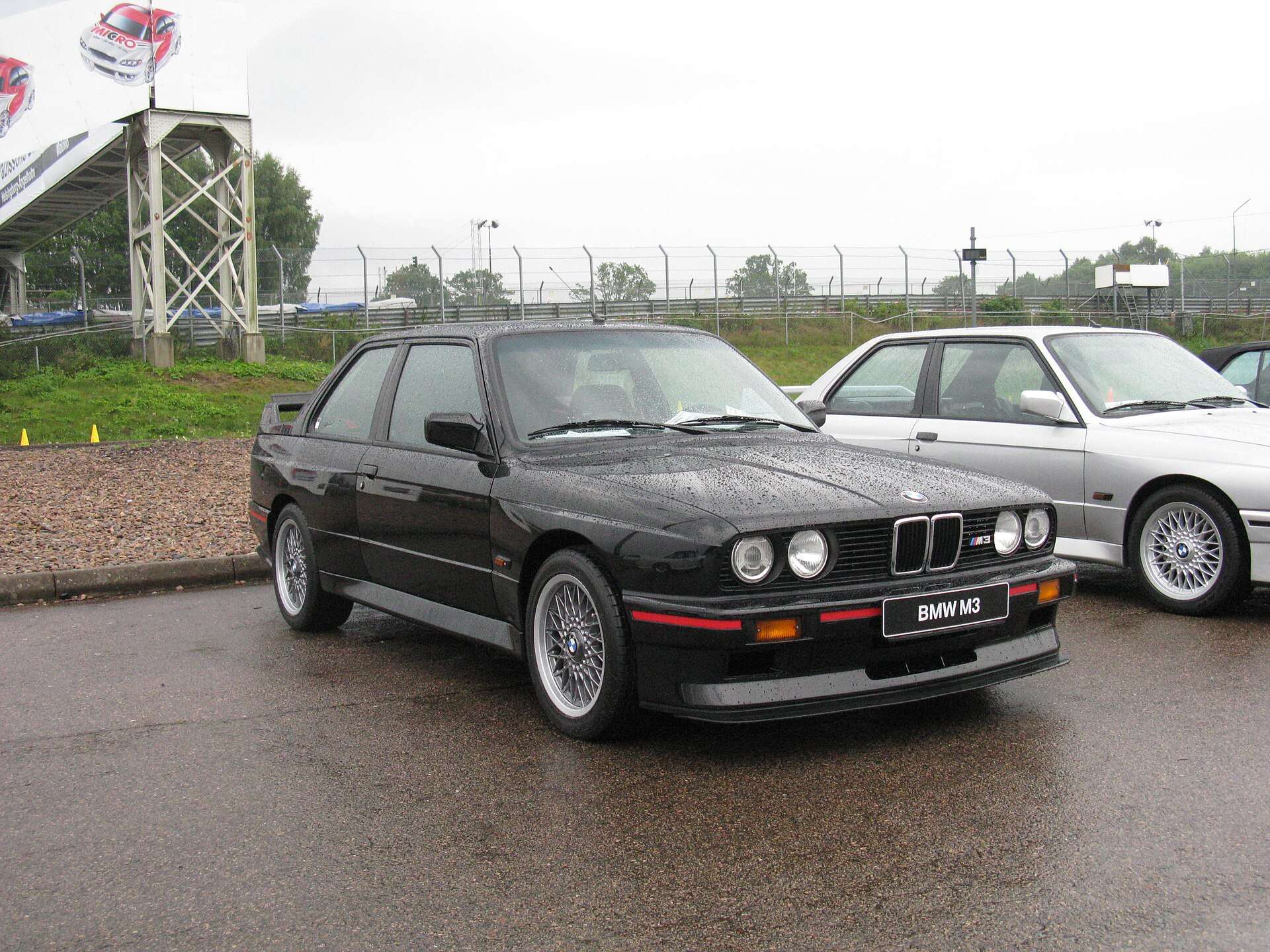 Black BMW E30 M3 Sport Evolution parked on wet pavement with an M3 number plate