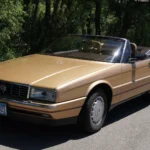 Gold 1987 Cadillac Allanté convertible with the top down, parked on pavement, front three-quarter view
