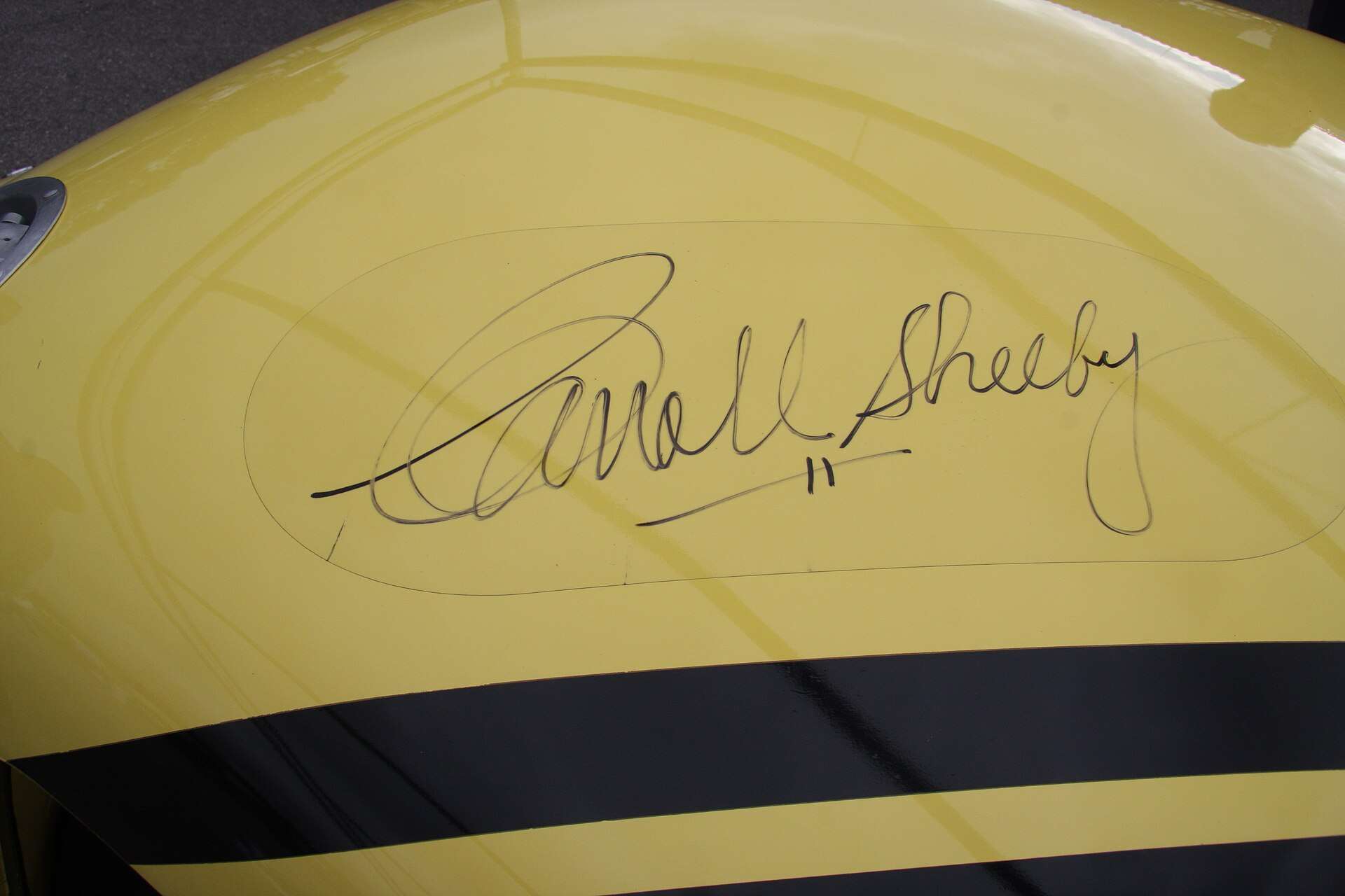 Carroll Shelby autograph in black marker on a cream-painted car panel
