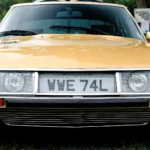 Citroën SM Buying Guide: Which Maserati-Powered Citroën to Buy, and What It Will Cost to Own Front view of a gold Citroën SM coupe with its glass-covered six-lamp nose parked on grass