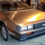 Front three-quarter view of an unpainted stainless-steel 1983 DeLorean DMC-12 on a showroom floor