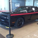 Black 2023 Dodge Challenger SRT Demon 170 on display behind stanchions and a red rope in a dealership showroom