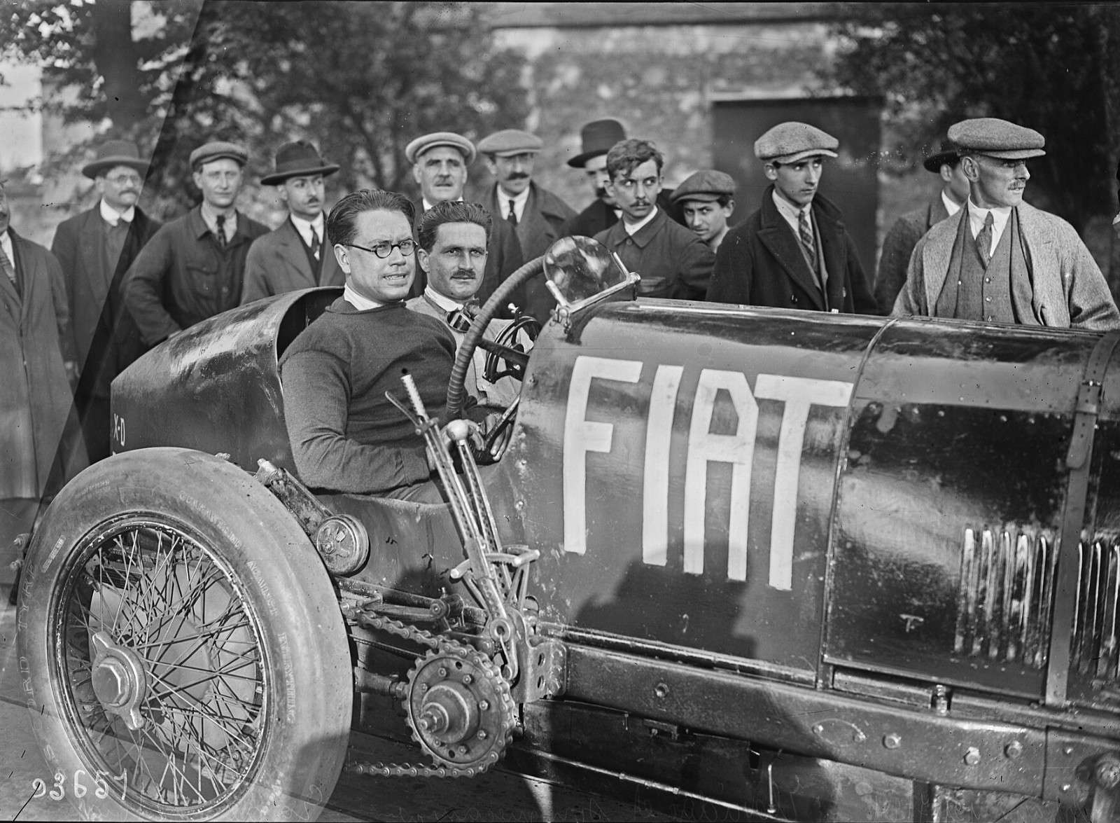 1924 photograph of Ernest Eldridge, wearing round glasses, seated in the Fiat Mephistopheles beside his mechanic with onlookers in flat caps behind and the FIAT name on the bodywork
