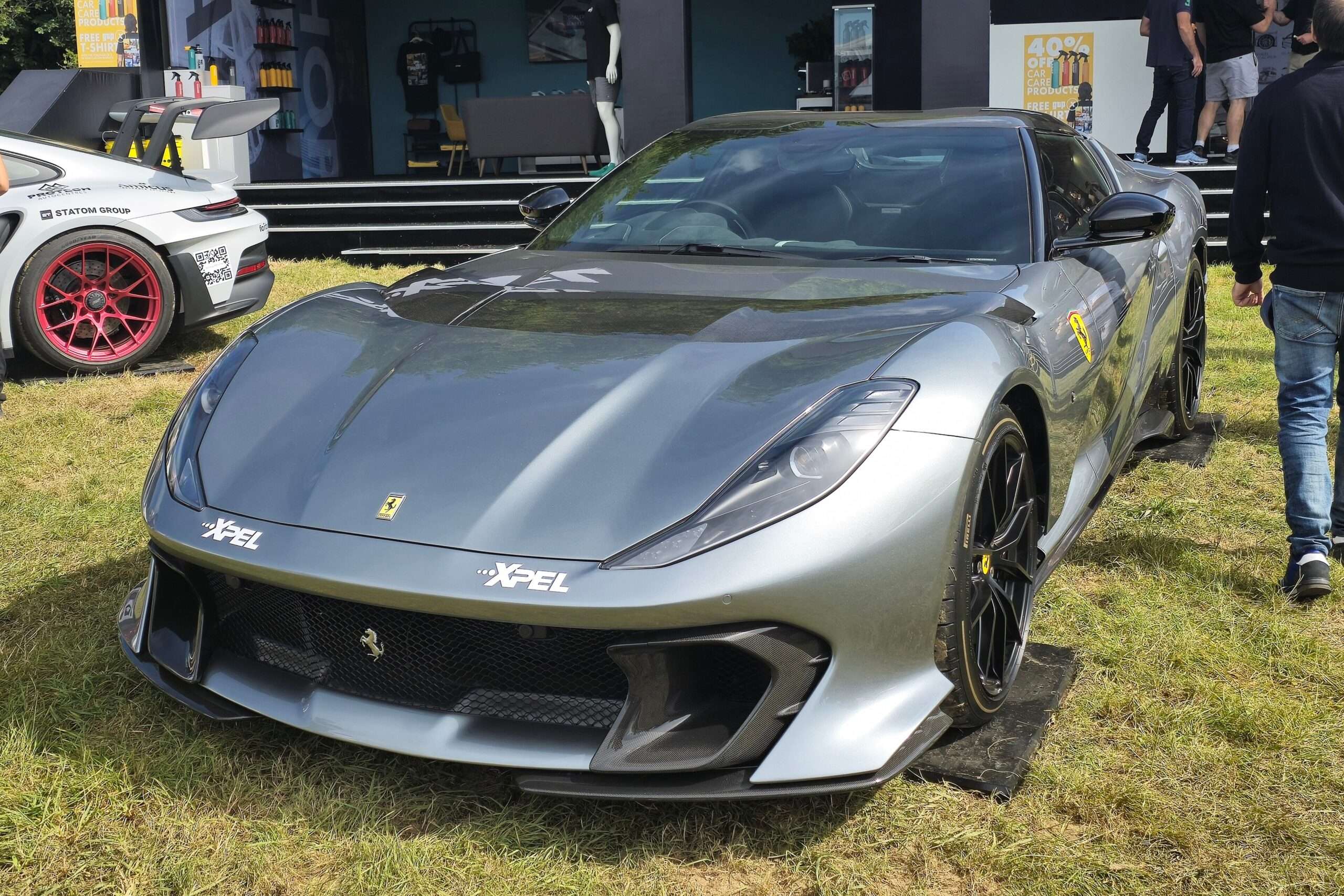 Grey Ferrari 812 Competizione at an outdoor event, front three-quarter view showing the carbon-fiber front splitter