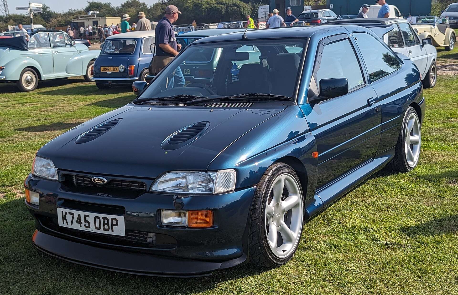 Dark blue Ford Escort RS Cosworth with twin hood vents and front splitter parked on grass at a car show