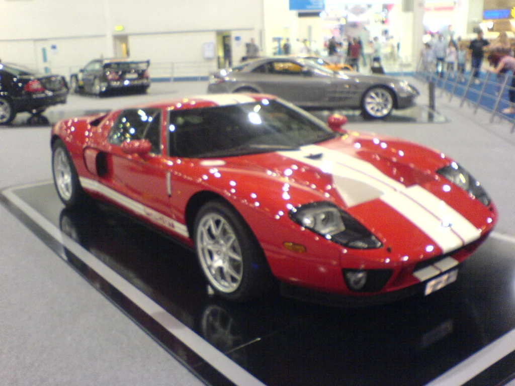 Red mid-engine coupe with white stripes, rear three-quarter view at a motor show