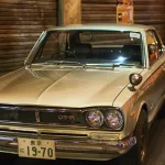 On a Hakosuka GT-R, Originality Lives in the S20 and the Plate, Not the Flares Silver Nissan Skyline 2000GT-R KPGC10 coupe, front three-quarter view, displayed in a Tokyo historic car collection