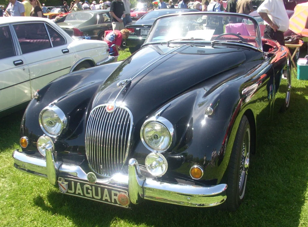 Black 1958 Jaguar XK150 roadster parked on grass at a car show