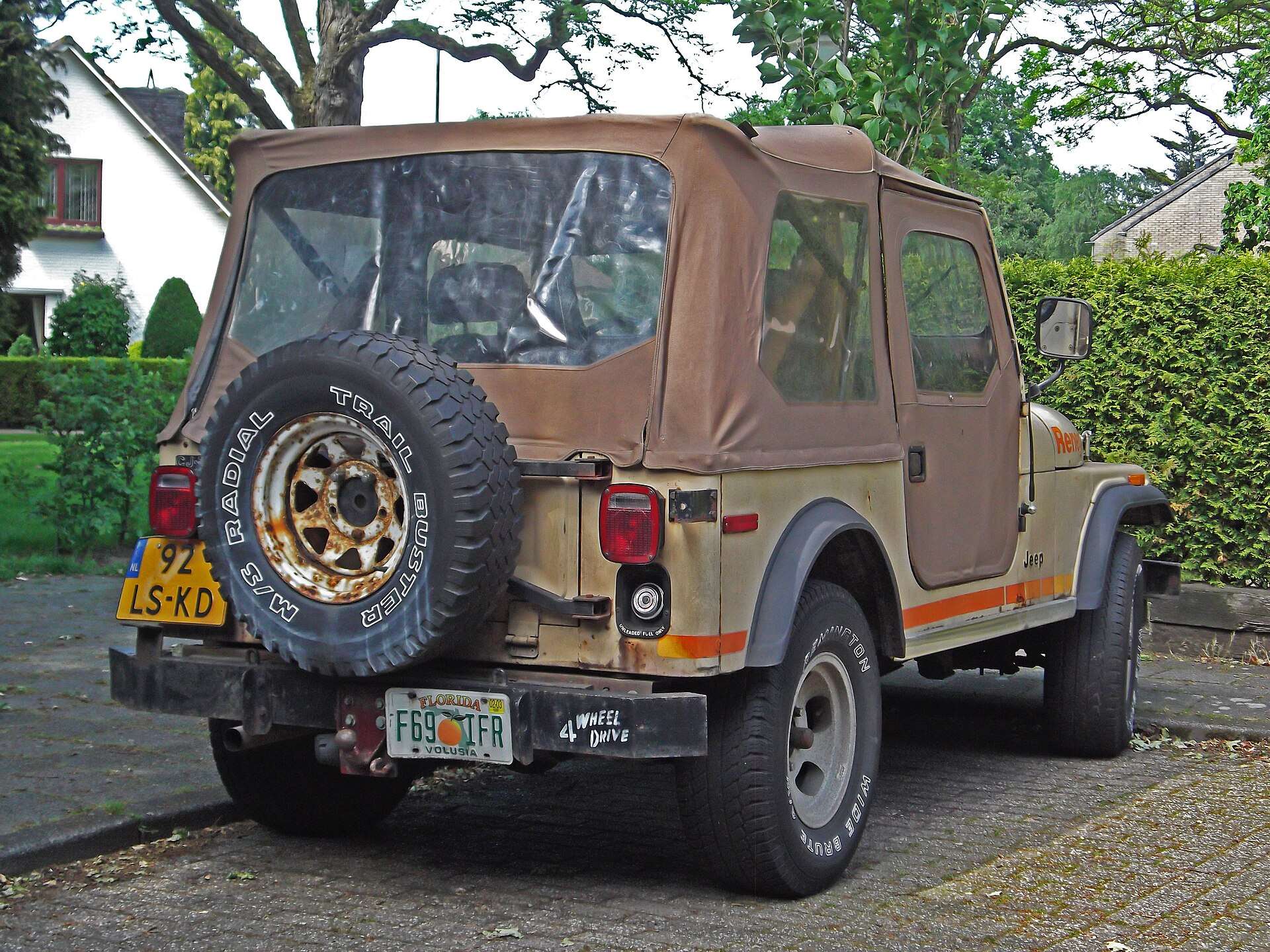 Rear view of a Jeep CJ-7 with tan soft top and a rear-mounted spare tire