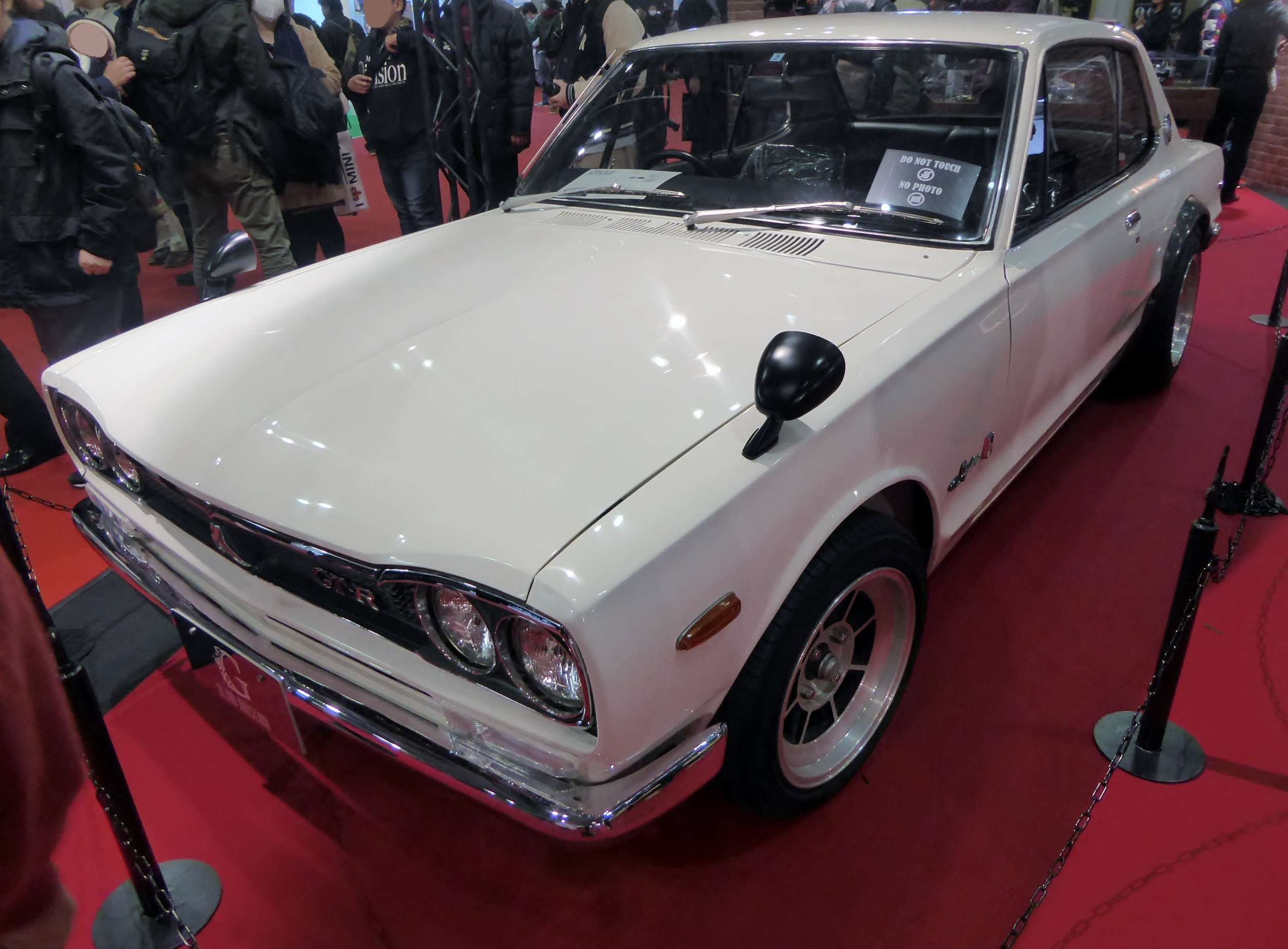 White Nissan Skyline 2000GT-R KPGC10 coupe at the Osaka Motor Show with fender-mounted mirrors and black rear-arch flares