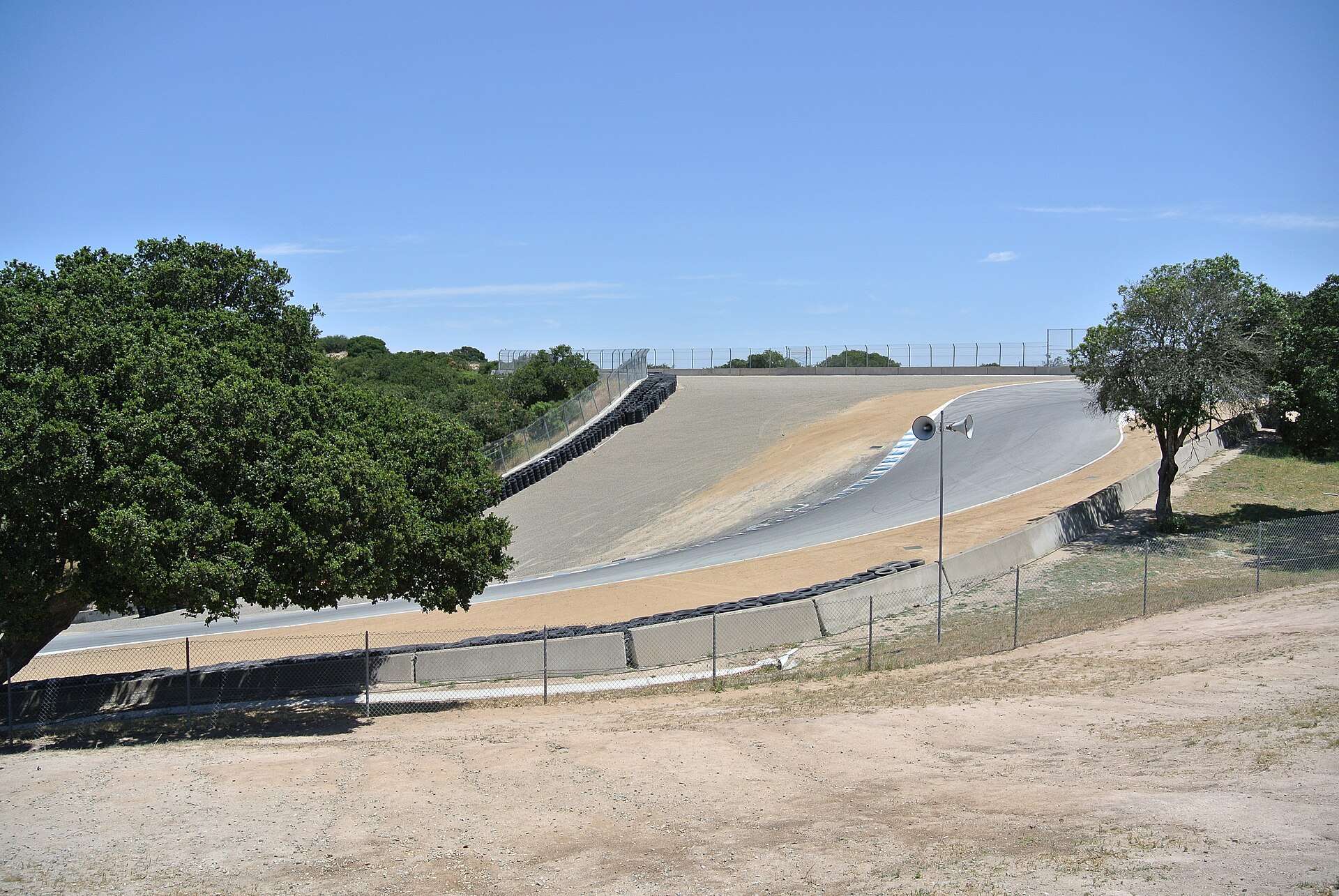Uphill view of the Corkscrew section of Laguna Seca Raceway in Monterey, California, with trees and a dry hillside