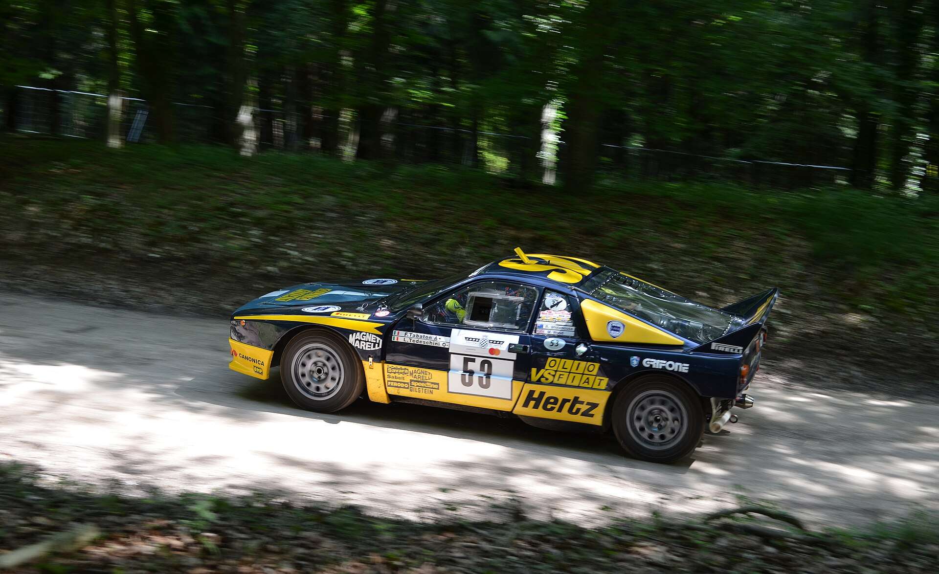 Lancia 037 Evo 2 driving through woodland showing the bumperless rear with mudflaps