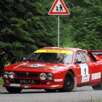 Lancia 037 rally car in red and white livery cornering on a tarmac stage at a historic rally