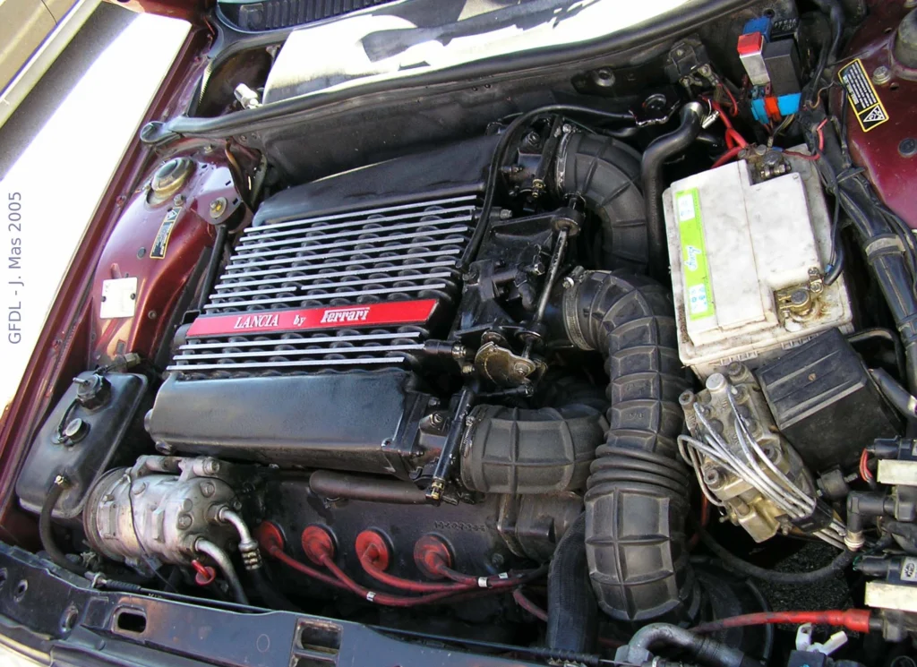 Top view of the engine bay of a Lancia Thema 8.32 showing the V8, red ignition leads, intake plumbing and ancillaries