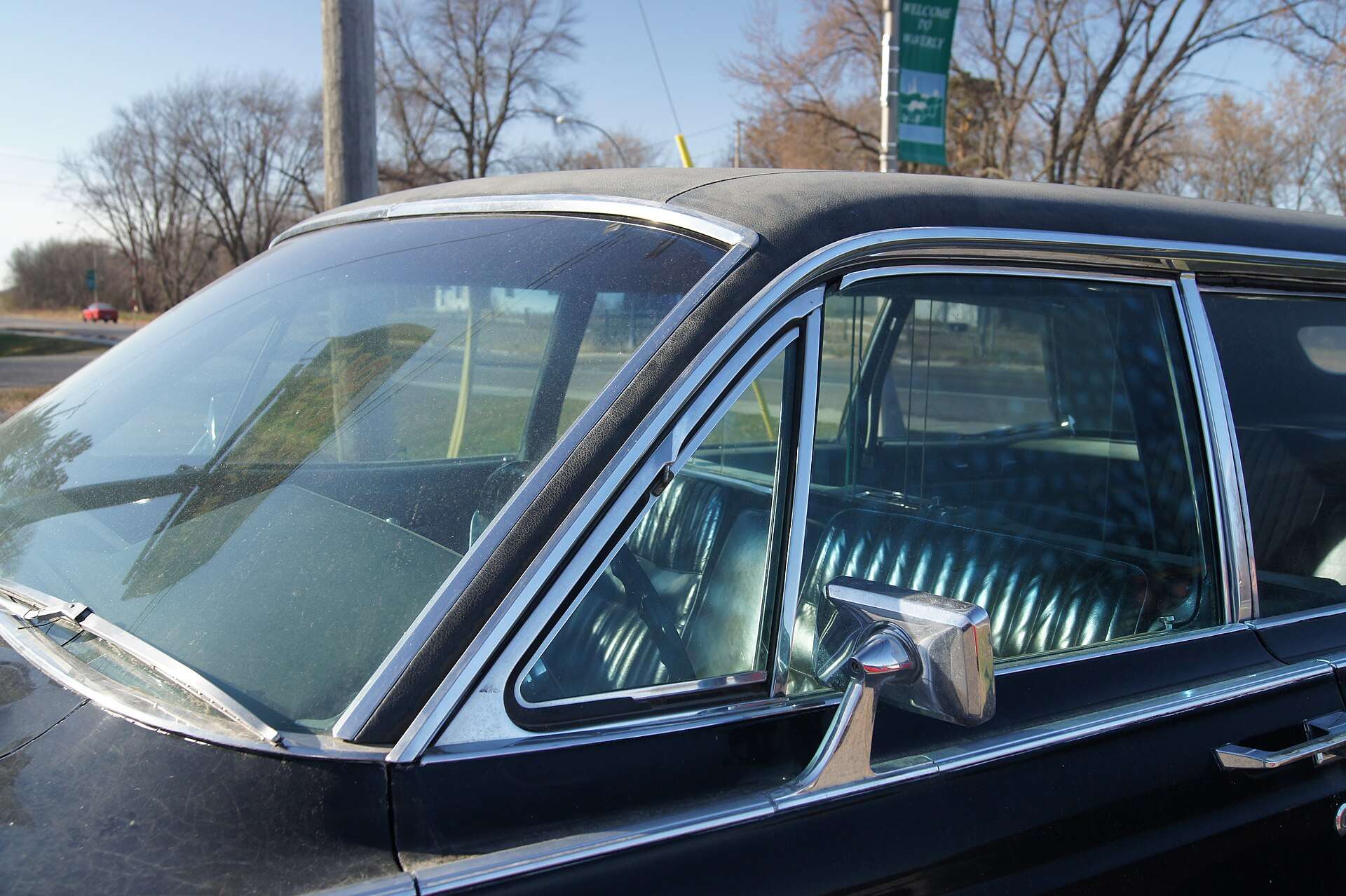 Close view through the front window of a black Lincoln Continental limousine showing a teal-green pleated upholstery in the passenger compartment