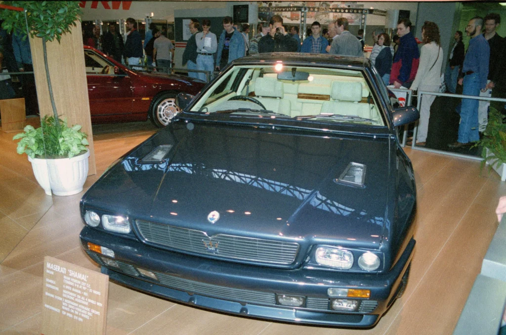 Dark blue Maserati Shamal displayed indoors at a motor show seen head-on with its multiple headlamps and grille