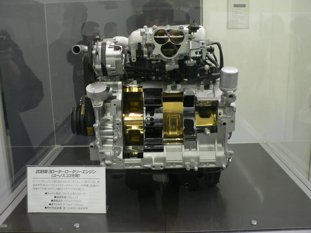 Cutaway display of the Mazda 20B-REW three-rotor engine showing the three rotor housings in a glass case